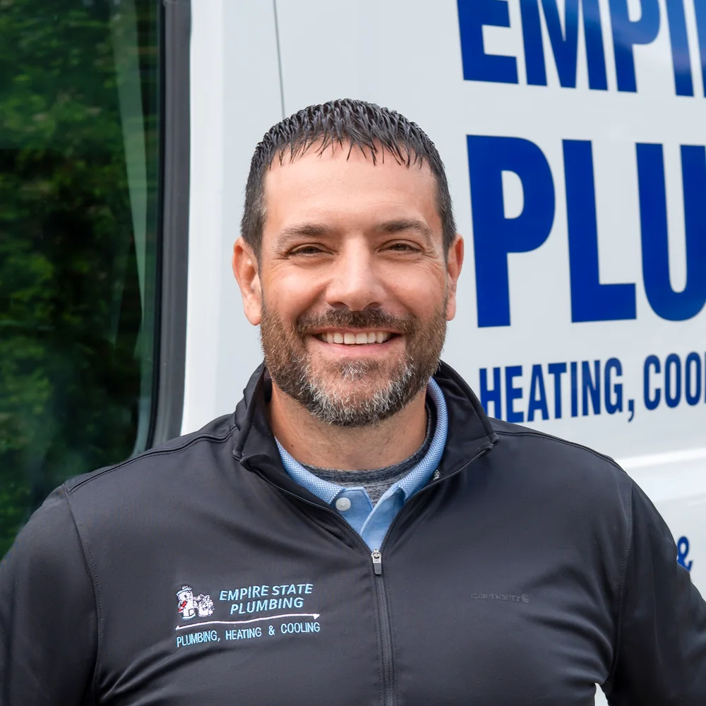 Empire State Plumbing service technician standing in front of a company service van