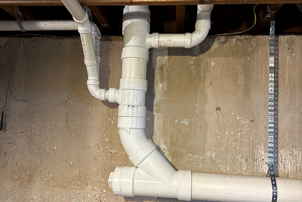 Clean new white PVC drain piping neatly installed along a basement wall by Empire State Plumbing