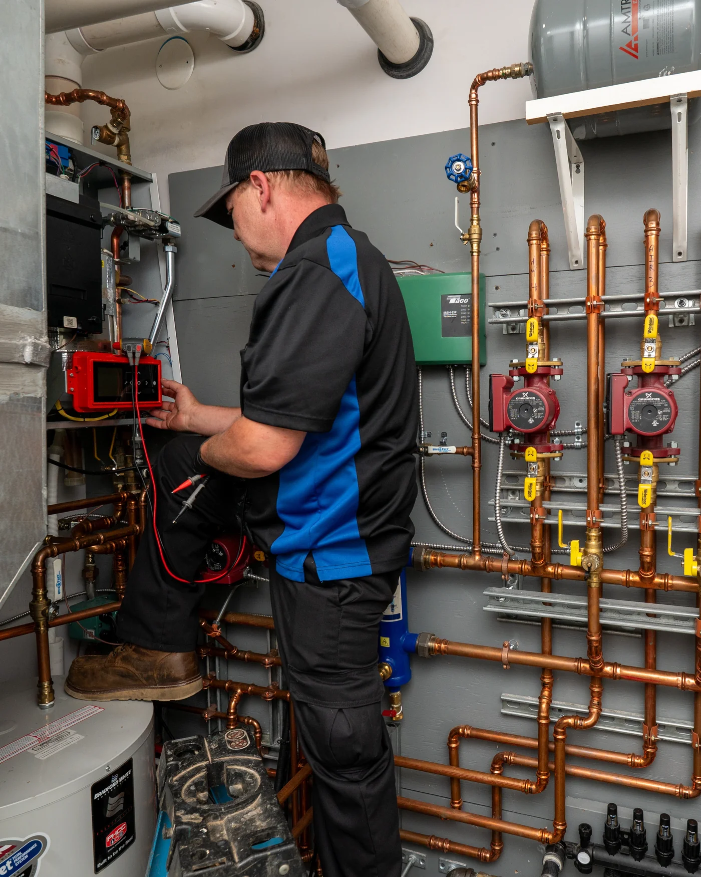 Empire State Plumbing technician using a multimeter to diagnose a boiler and water heater system with copper piping